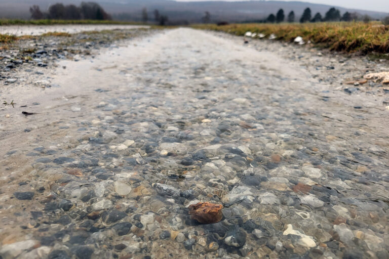 Wasser fließt über einen geschotterten Wirtschaftsweg ab